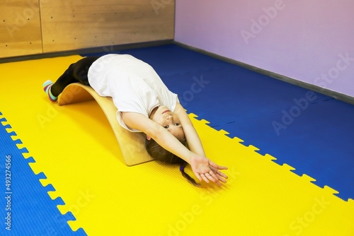 a little girl in a white T-shirt lies on a medical balance beam in a rehabilitation center and undergoes a course