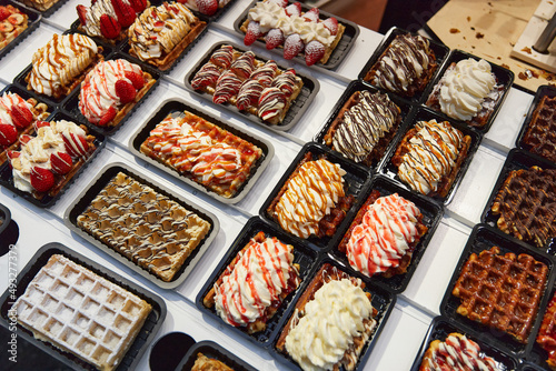 Various of traditional Belgian waffles topped with chocolate, speculoos, whipped cream and fruit display in a storefront in Brussels