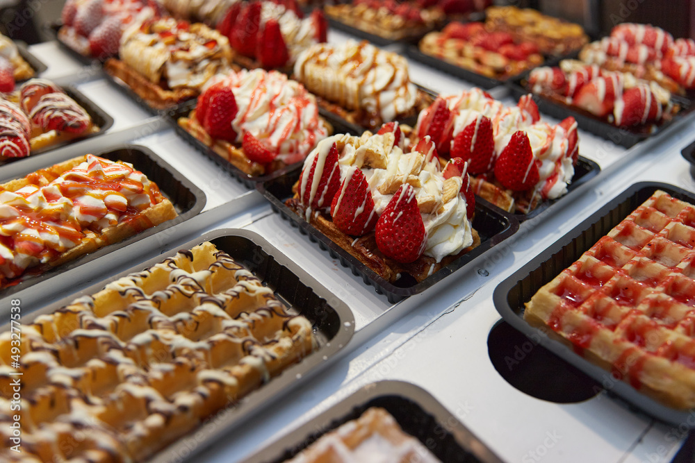 Various of traditional Belgian waffles topped with chocolate, speculoos, whipped cream and fruit display in a storefront in Brussels