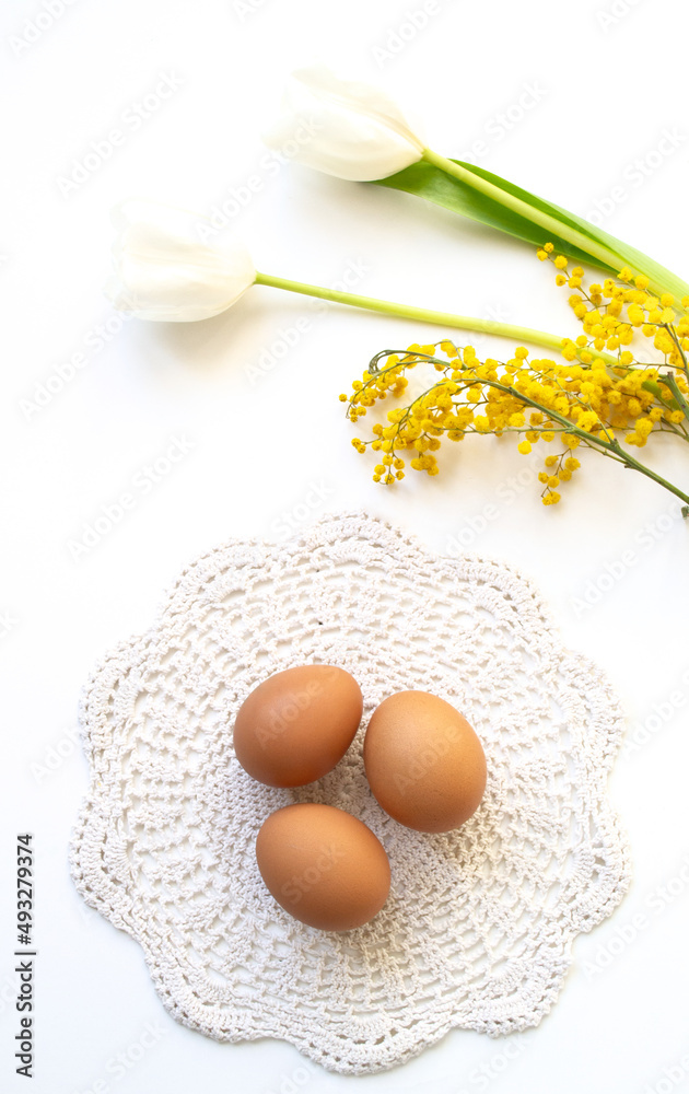 Easter banner. Easter eggs in a wooden plate in the sunlight with tulips and mimosa on a white background
