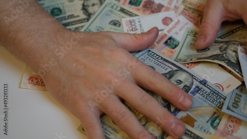 Male hands are raking and pulling a lot of money from Russian and American banknotes, close-up. Greed, bribery and corruption