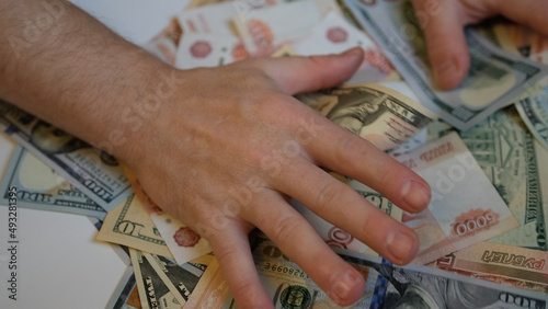 Male hands are raking and pulling a bunch of money from Russian and American bills, close-up. Greed, bribery and corruption