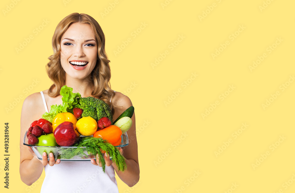 Studio portrait image of excited happy smiling young blond woman holding glass plate with vegetarian food. Healthy eating, dieting concept, isolated over yellow color background Studio portrait image of excited happy smiling young blond woman holding glass plate with vegetarian food. Healthy eating, dieting concept, isolated over yellow color background