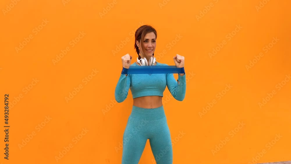 Atractiva mujer deportista haciendo ejercicios físicos con una banda elástica sobre un fondo de color naranja	