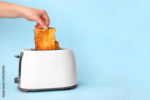 Woman taking bread slice from toaster on blue background