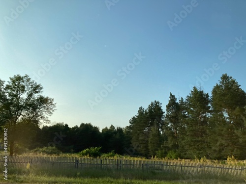 Photo of the fence in the village with green trees and blue sky
