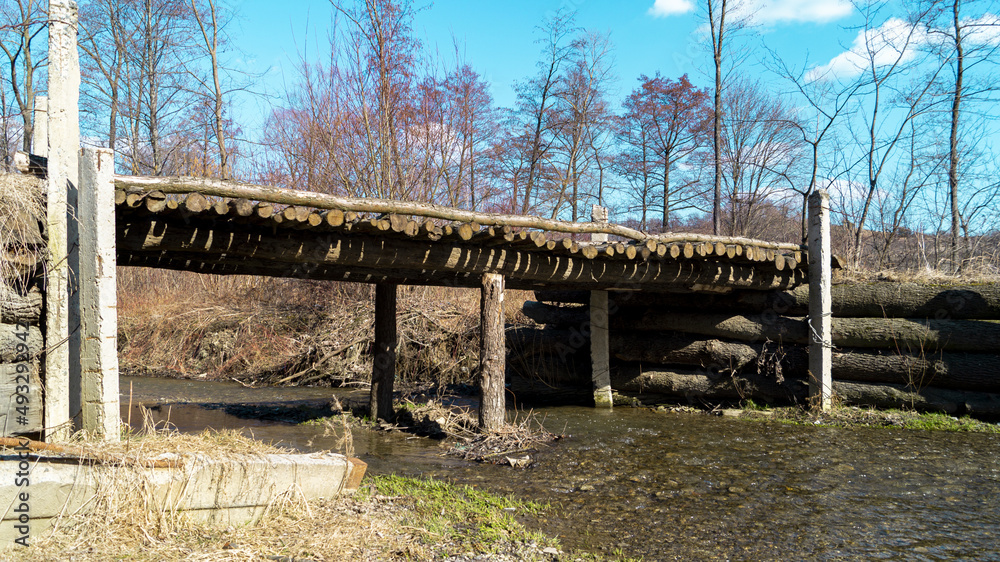 An old bridge made of wooden logs across a shallow river
