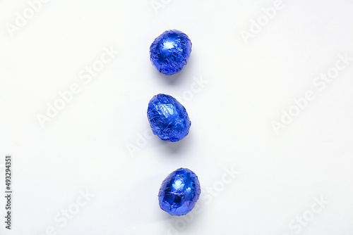 Tasty chocolate eggs in blue foil on white background