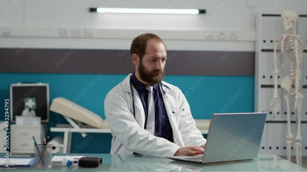 Portrait of male physician wearing white coat and using laptop at desk, working on consultation appointment to treat patients. Specialist smiling and feeling confident about medical expertise. Portrait of male physician wearing white coat and using laptop at desk, working on consultation appointment to treat patients. Specialist smiling and feeling confident about medical expertise.