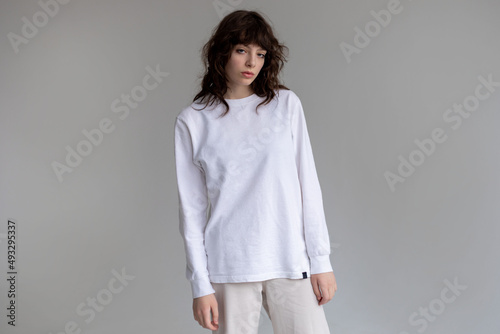 Young woman with curly hair in a white long sleeve t-shirt stands on a white background. Mock-up. photo
