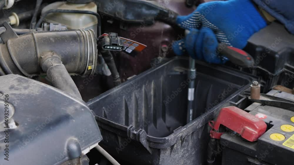 Car Engine Repair. Hands of an auto mechanic in blue ratchet key gloves unscrew the air filter housing under the hood of the car Car Engine Repair. Hands of an auto mechanic in blue ratchet key gloves unscrew the air filter housing under the hood of the car