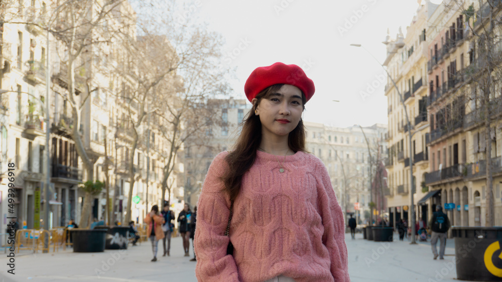 Mujer asiatica con gorro rojo y sueter rosa posa en una calle de Barcelona en invierno
