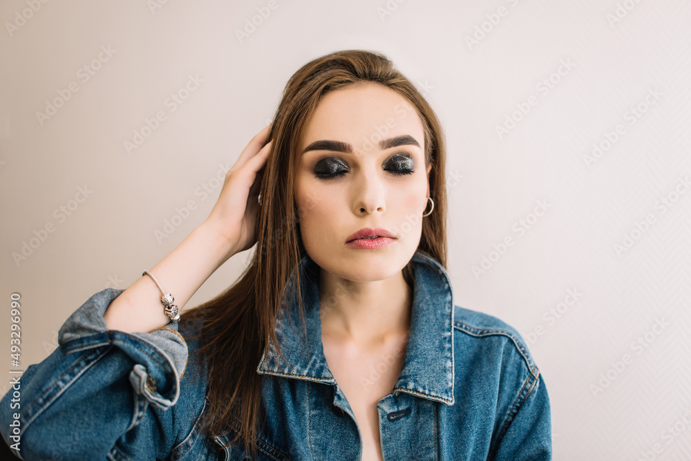 Young brunette girl wearing denim jacket. Bright evening makeup, smoky eyes, close up Young brunette girl wearing denim jacket. Bright evening makeup, smoky eyes, close up