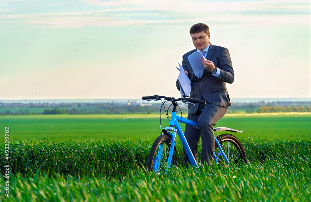 businessman dressed in a business suit, rides with reports or documents a bicycle through a green grass field, beautiful nature in spring, business concept businessman dressed in a business suit, rides with reports or documents a bicycle through a green grass field, beautiful nature in spring, business concept