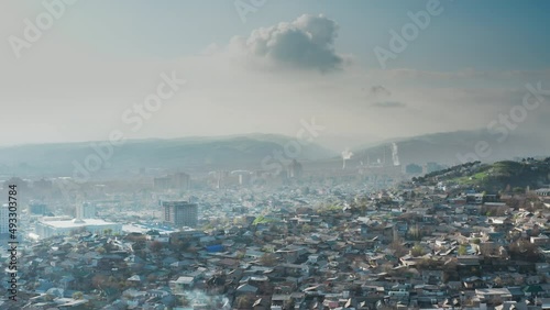 Beautiful urban landscape city with factories from pipes of which heavy smoke is pouring against background of green mountains in fog. Outskirts of city in bird's-eye view of Dushanbe. Tajikistan. photo