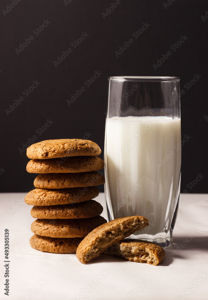A glass of milk and oatmeal cookies stacked on top of each other. Oatmeal cookies broken in half. A glass of milk and oatmeal cookies stacked on top of each other. Oatmeal cookies broken in half.