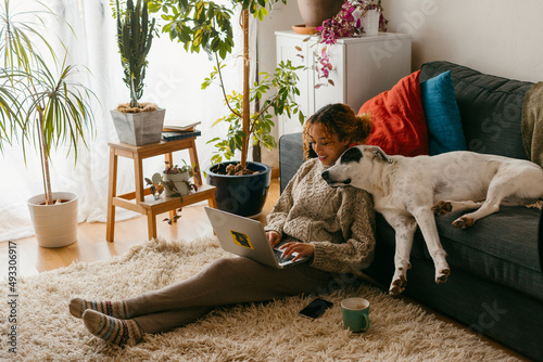 Teenager at home with dog relaxing while using laptop