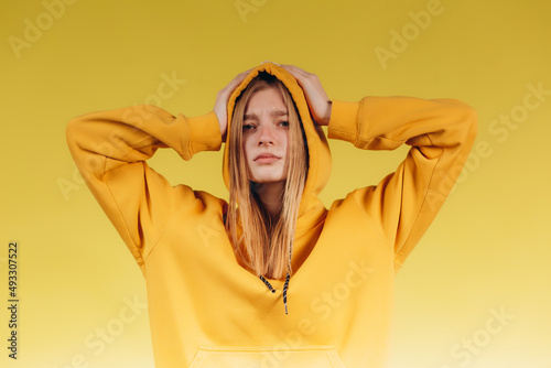 Portrait of sad young teen girl holding hands on head, wearing casual yellow hoodie in tone with background © Igor