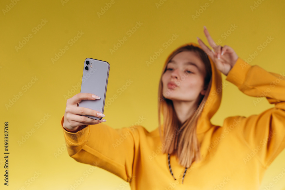 woman taking selfie on yellow background. The teenager is dressed in a yellow skinny. The girl is happy