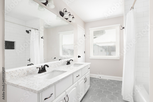 A renovated bathroom with a white vanity, grey hexagon tiled floor, marble countertop, and a shower with white subway tiles.
