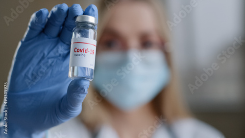 Close-up female specialist chemist biochemist woman doctor nurse scientist in medical mask glasses and latex gloves looking at camera holding bottle of covid vaccine coronavirus vaccination concept