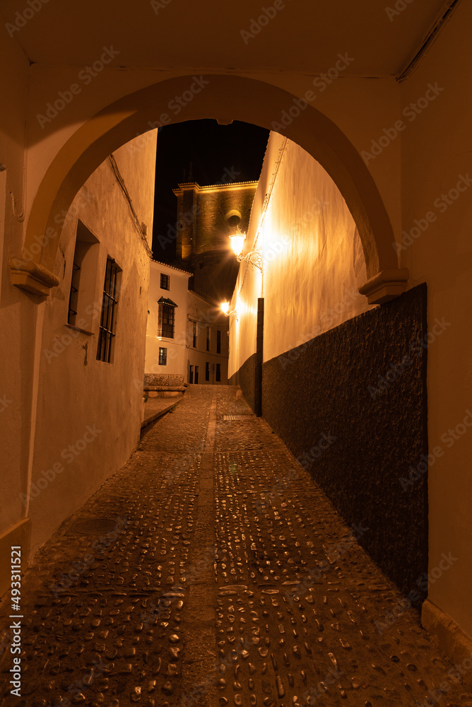 Narrow street in the old town of the white village of Ronda with the church of Santa Maria la Mayor in the background at night, Malaga province, Andalusia, Spain Narrow street in the old town of the white village of Ronda with the church of Santa Maria la Mayor in the background at night, Malaga province, Andalusia, Spain