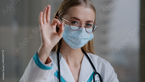 Portrait caucasian doctor specialist therapist nurse surgeon woman girl in glasses in medical protective face mask looking at camera showing ok gesture excellent perfect fine well good success sign