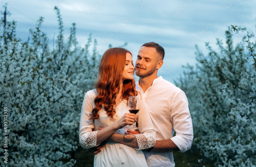 Romantic date in bloom in the evening. Loving couple with wine glasses on a flowering background. Romantic date in bloom in the evening. Loving couple with wine glasses on a flowering background.