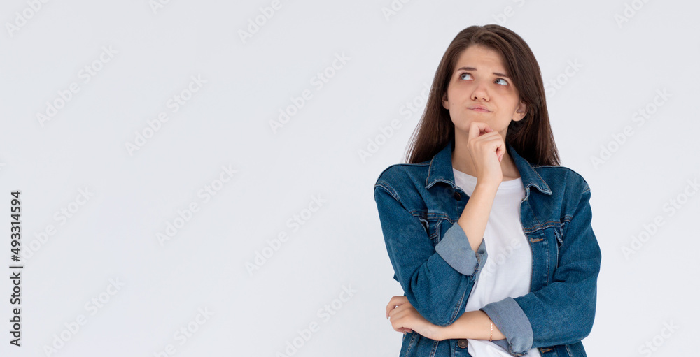 Close up portrait of pretty confident thoughtful girl, holding hand near the face, looking seriously up, standing over grey background with copy space
