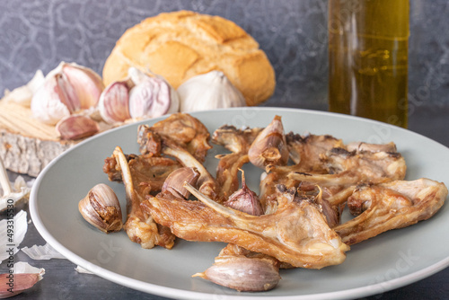 Dish of young goat ribs fried with garlic, a typical Spanish dish, on a wooden background.