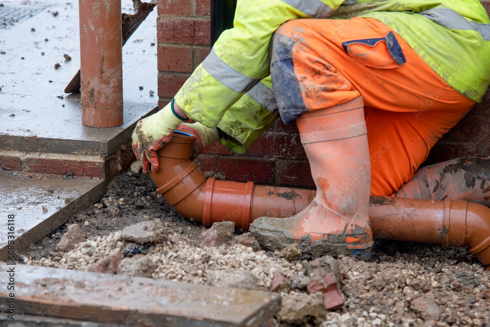 Groundworker fitting plastic drainage pipe to connect new build house