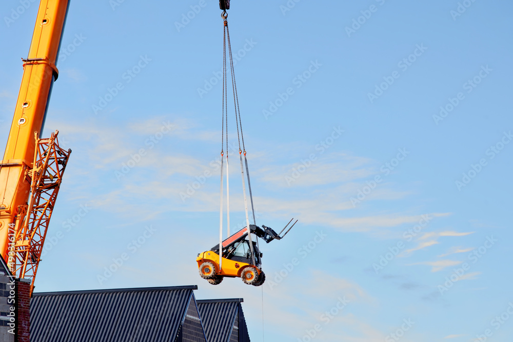 Mobile crane lifting forklift above the building to place it in the ...