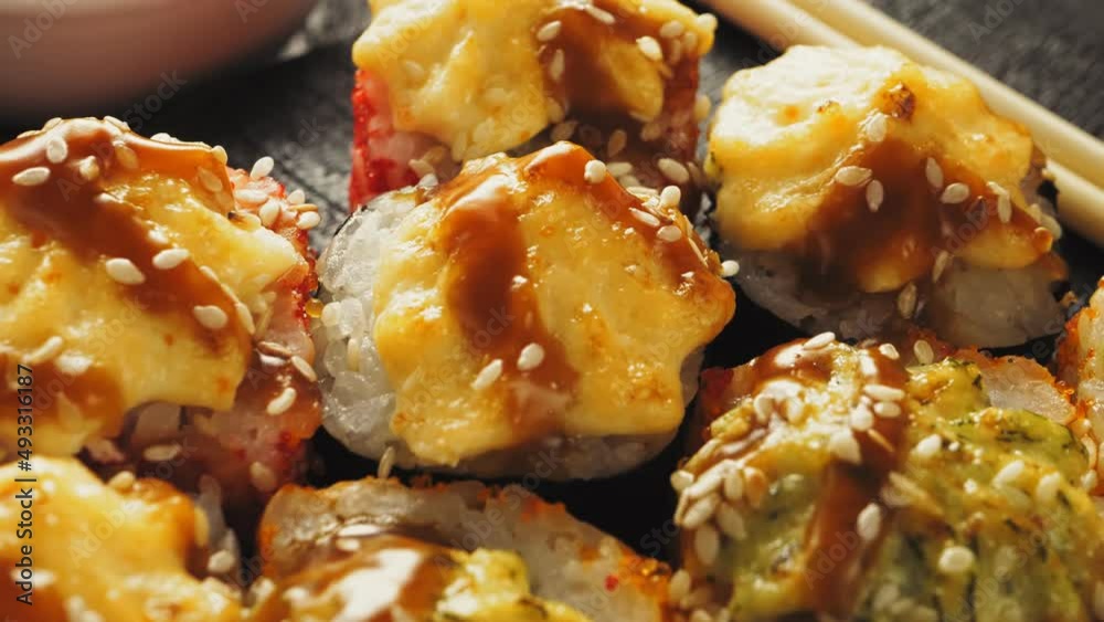 Roll baked in teriyaki sauce is taken with chopsticks from a black wooden board Roll baked in teriyaki sauce is taken with chopsticks from a black wooden board