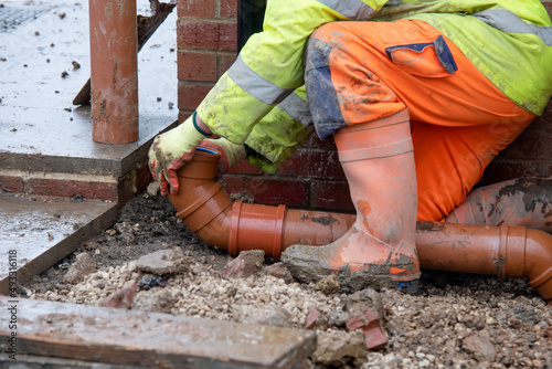 Groundworker fitting plastic drainage pipe to connect new build house to the underground drainage network photo