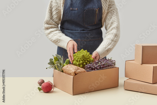 Woman in apron packing fresh vegetables in box photo