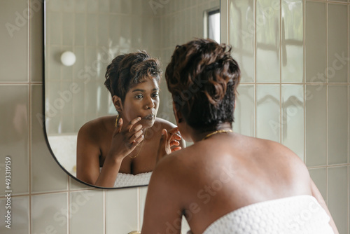 Young woman inspecting a facial blemish in a mirror