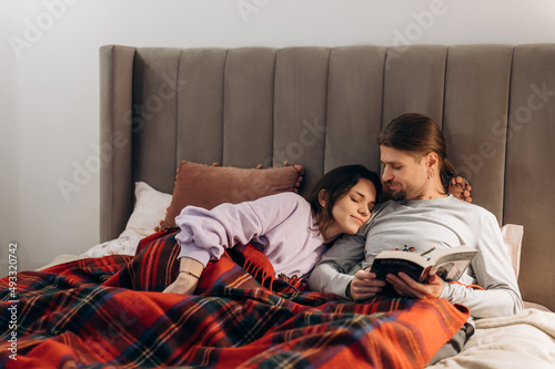 Couple reading book in bed under plaid photo