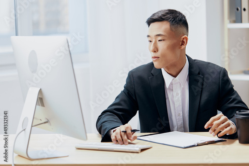 Asian man in a suit glass of coffee sits at a tablein front of a computer technologies
