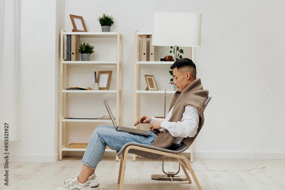 Asian man on a laptop in a chair in a freelance room technologies