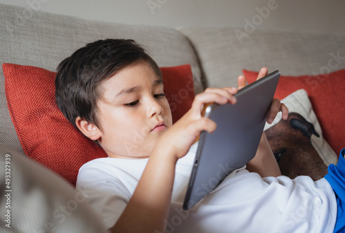 School boy using tablet studying online on internet, Kid playing game or watching cartoon on digital pad, Happy Child relaxing at home, Children with technology and social network concept