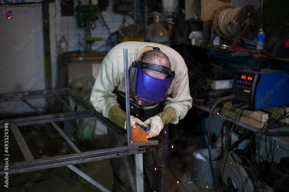 Welder at work. The welder heats the metal. Classes in the workshop. Steel processing. Welder in a blue welding mask. Welder at work. The welder heats the metal. Classes in the workshop. Steel processing. Welder in a blue welding mask.