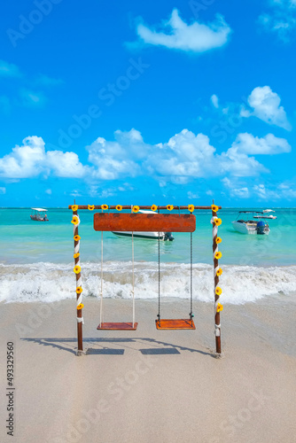 Two seat swing decorated with sunflower flowers on a beautiful beach of fine sand and cyan-toned sea on a beautiful blue sky day. Landscape of Maragogi beach, Alagoas state, Brazil.