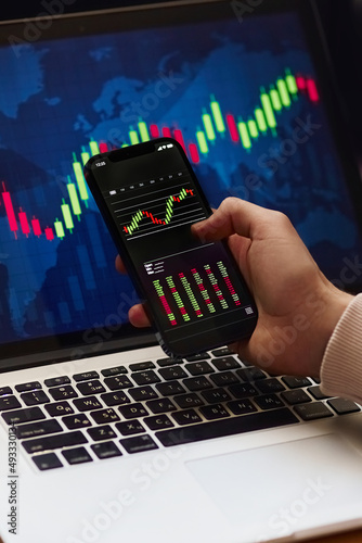 Businessman investor analyst using mobile phone analytics to analyze crypto currency financial market, trade data index chart graph on smartphone and laptop screen. close-up