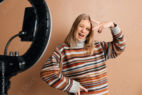 The girl is having fun while making photos for her blog. Young woman is using a mobile phone and a ring light to take photos. Concept of blogging photo