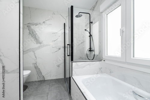 Bathroom with bathtub, individual shower cabin with black accessories and marble tiling on the walls