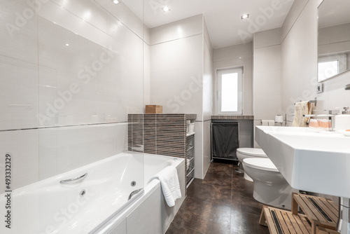 Bathroom with white bathtub with glass partition  angular white porcelain sink and brown tiled work furniture