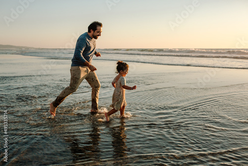 Father chasing daughter in ocean at sunset