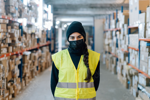 Woman wearing mask standing between racks in warehouse