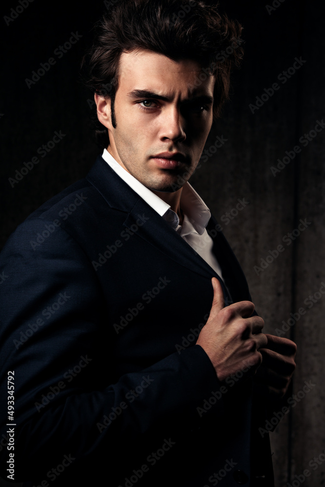 Fototapeta premium Charismatic handsome male in blue fashion suit and white style shirt sad looking down on dark shadow background. Closeup studio