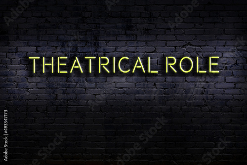 Night view of neon sign on brick wall with inscription theatrical role